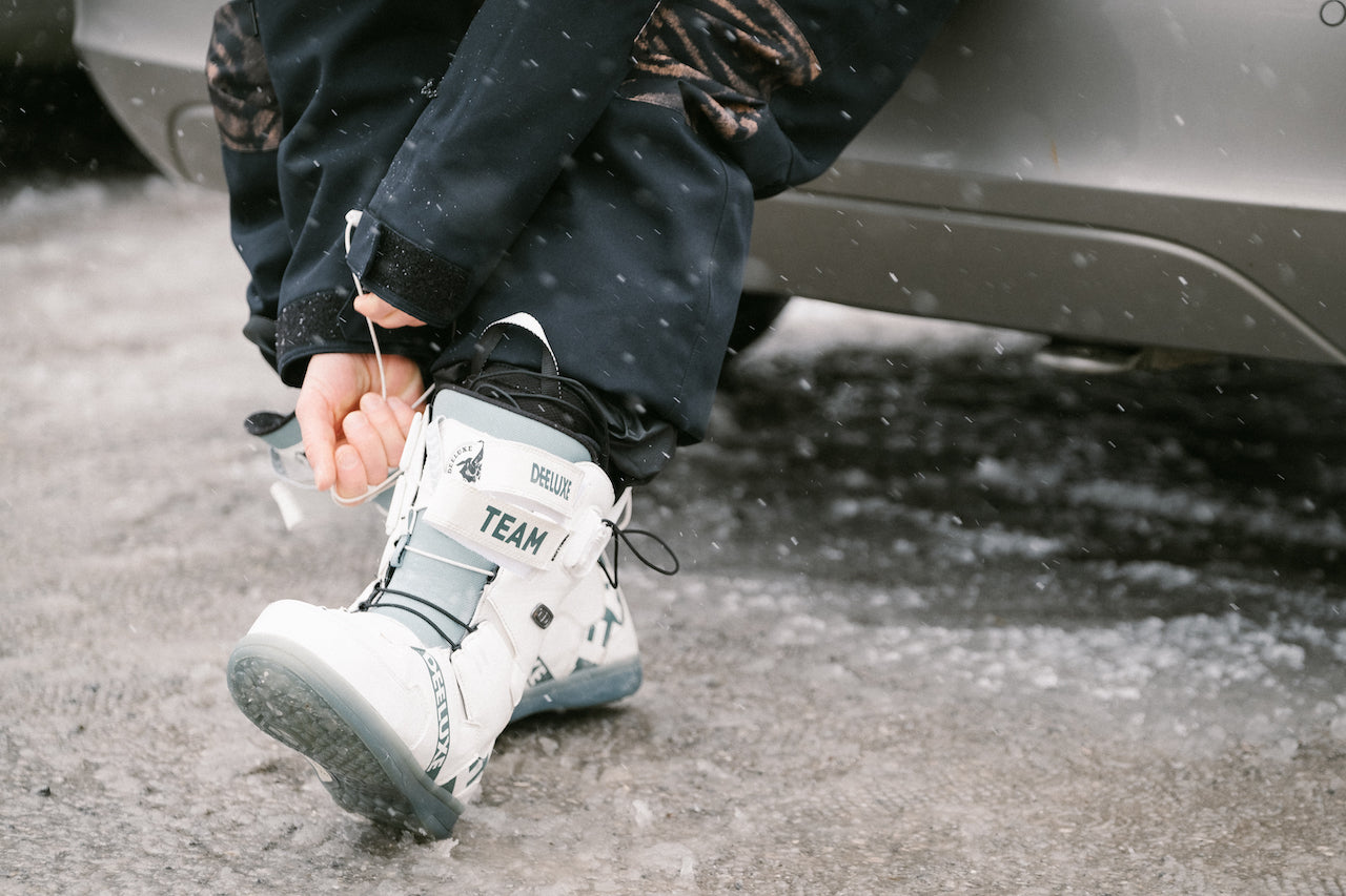 Snowboarder lacing up snowboard boot outside vehicle
