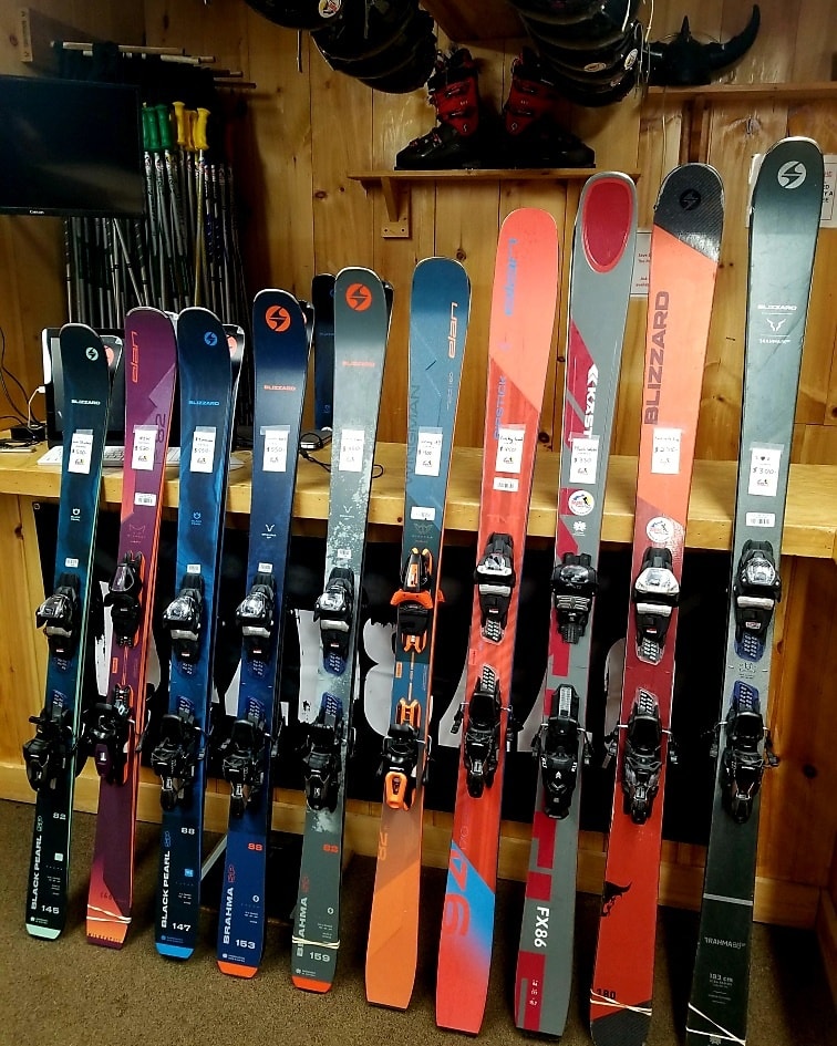 Lightly used demo skis lined up inside ski shop, ready for sale