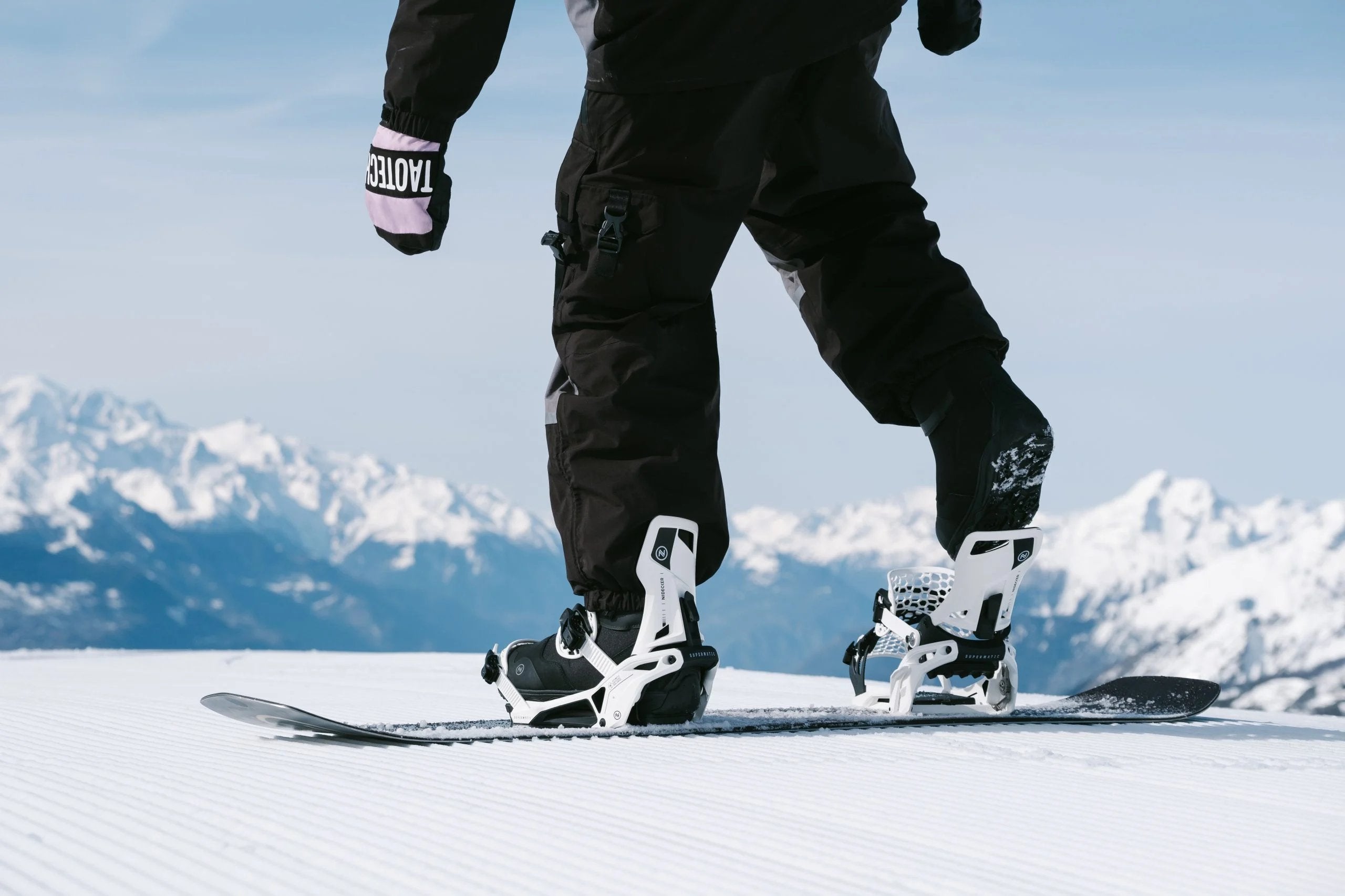 Snowboarder stepping into Nidecker binding on top of mountain
