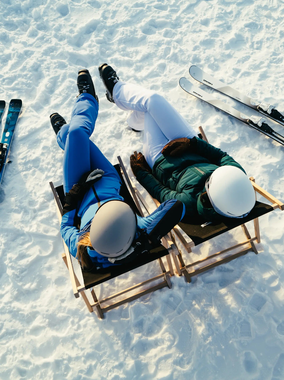 Two female skiers sitting in lounge chairs on snow next to Head Skis.